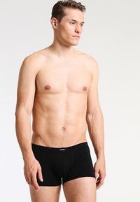 Boxer in cotone nero realizzati in tessuto elasticizzato, con una vestibilità aderente e un logo sulla vita. Il modello è in piedi con un'espressione neutra.