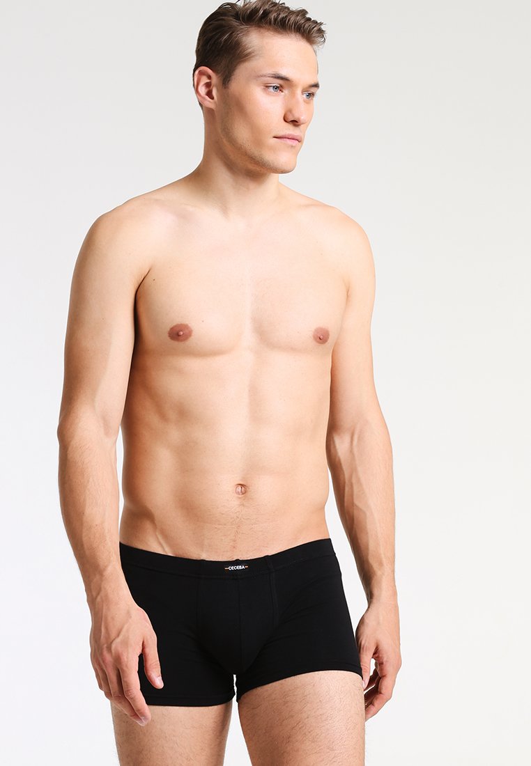 Boxer in cotone nero realizzati in tessuto elasticizzato, con una vestibilità aderente e un logo sulla vita. Il modello è in piedi con un'espressione neutra.