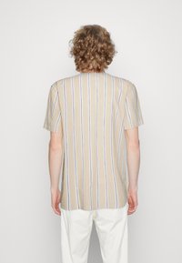 Chemise à manches courtes beige avec des rayures verticales blanches et bleu marine, fabriquée en tissu doux. Ourlet droit avec une coupe décontractée, peu de détails de couture.