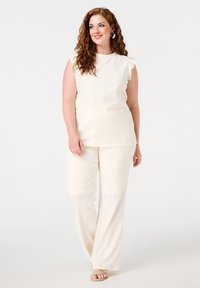 Ensemble en tricot de couleur crème comprenant un haut à manches courtes volantes et un pantalon large avec un motif texturé et un subtil design en open weave.