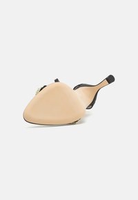 Black high-heeled shoe with a pointed toe and textured upper, featuring a nude sole and a decorative accent near the toe.