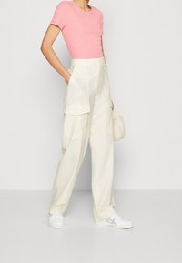 Top corto a maniche corte color rosa chiaro a coste abbinato a pantaloni cargo color crema con grandi tasche, completato da sneakers bianche e una borsa piccola.