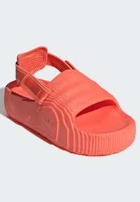 Coral-colored slide sandal with textured rubber material, open toe, wide strap, and adjustable closure. Features ribbed side design and logo.