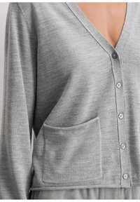 Cardigan grigio con scollatura a V, dotato di una singola tasca frontale, tessuto leggero e chiusura con bottoni. Texture liscia con dettagli di cucitura sottili.