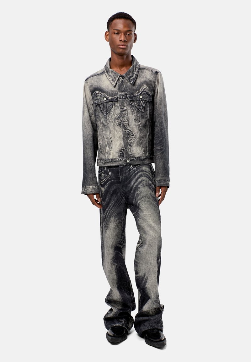 Giacca in denim nera e grigia con jeans coordinati, caratterizzata da un lavaggio sbiadito e dettagli di cucitura intricati. Il modello è in piedi su uno sfondo neutro.