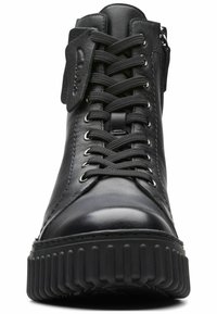 Zapatilla alta de cuero negro con puntera redonda, cuello acolchado, cierre de cordones y suela de goma texturizada con estrías.