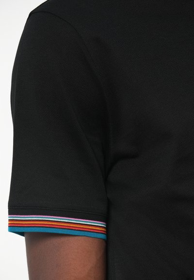 Melnā polo krekla izstrādājums no teksturēta auduma, ar daudzkrāsainu svītru aproci, kurā ir sarkanas, rozā, zilas un dzeltenas akcenti.