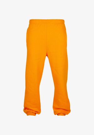 Jasnopomarańczowe dresy wykonane z miękkiego materiału, z elastycznym paskiem w talii i ściągaczami na kostkach. Brak widocznych kieszeni lub dodatkowych detali.