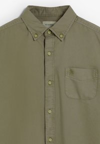 Camicia verde oliva con bottoni, realizzata in tessuto morbido. Presenta un colletto a punta, sei bottoni e una tasca sul petto con un logo ricamato.