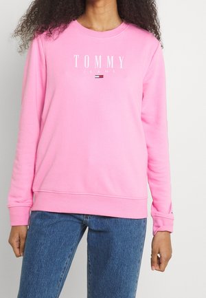 Sweatshirt en coton rose avec col rond, arborant le texte de logo blanc "TOMMY JEANS" et un petit détail de drapeau contrastant au centre.