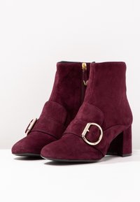 Burgundy mockaskinsstövlar med rund tå, klack i blockstil, sidodragkedja och guldfärgad spänne detalj på remmen över framsidan.