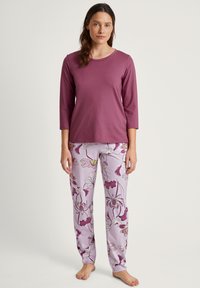 Paarse langesleeve top met ronde hals, gecombineerd met lichtlavendel pyjamabroek met bloemenpatroon en roze en gele accenten.