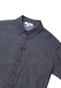 Chemise bleu foncé à boutons, avec un tissu texturé, dotée d'un col classique et de six boutons sombres sur le devant. Étiquette de marque visible.