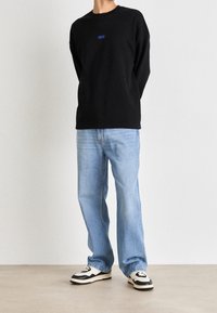 Svart långärmad tröja med blå "HUGO"-logga, ihopparad med ljusblå avslappnade jeans och svart-vita sneakers.