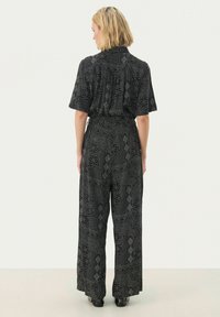 Black patterned jumpsuit featuring short sleeves, a cinched waist, and wide-leg pants with a textured print of shapes and lines.