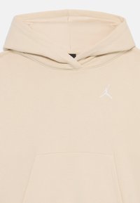 Bežs kapucis ar priekšējo kangarū mēteli un mazu baltu Jumpman logo uz kreisā krūts, ar kapuci bez auklām.