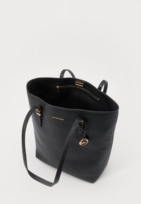 Sac fourre-tout en cuir noir avec des accessoires en or, à ouverture facile, avec des sangles réglables et un pendentif logo. L'intérieur comporte une poche zippée.