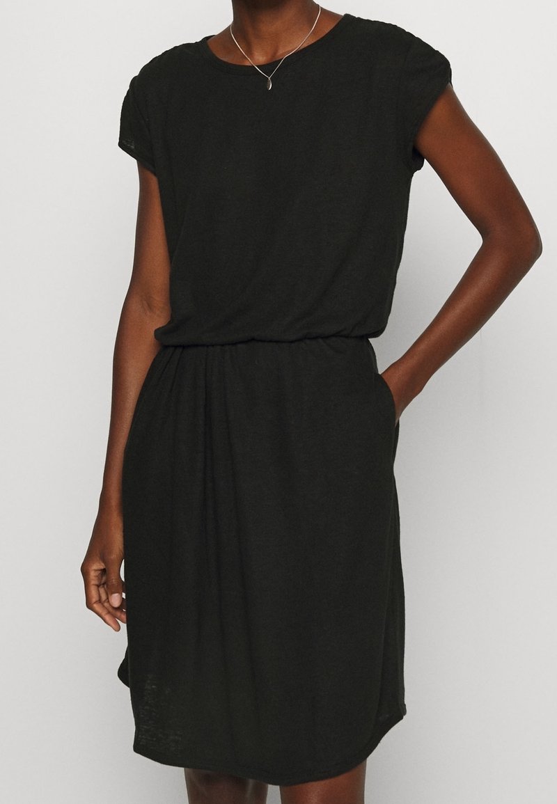Schwarzes, kurzärmeliges Kleid aus weichem Material, mit einem lockeren Schnitt, gerafftem Tailleneinsatz und seitlichen Taschen. Einfacher Rundhalsausschnitt und glatte Textur.