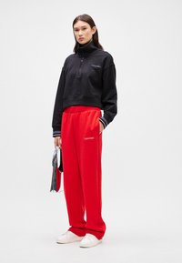 Czarny krótki sweter z zamkiem na szyi i białymi paskami na mankietach, w połączeniu z luźnymi, czerwonymi spodniami dresowymi z logo Calvin Klein. Białe sneakersy.