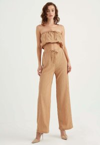 Bezramkowy, marszczony beżowy top crop połączony z spodniami o wysokim stanie i szerokich nogawkach. Oba elementy mają teksturowany materiał i ściągacz w talii.
