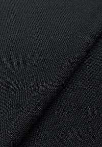 Zwarte gebreide stof met een fijne textuur en een regelmatig patroon, gevouwen om het gladde oppervlak en de diepte te tonen.