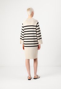Abito in maglia beige con strisce orizzontali nere, di lunghezza media, colletto rotondo e maniche lunghe; abbinato a sandali leggeri.