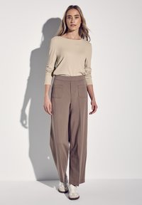 Beige ribbed pitkähihaine paita yhdistettynä leveälahkeisiin taupe-housuihin, joissa on kaksi etutaskua, ja niitä on yhdistetty valkoisiin ja harmaisiin tennareihin.
