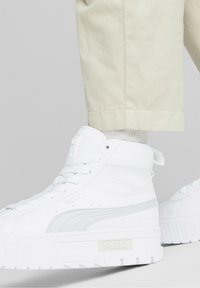 Sneaker alte bianche con pelle testurizzata e dettagli lisci, caratterizzate da una suola bianca spessa e un logo sul lato.