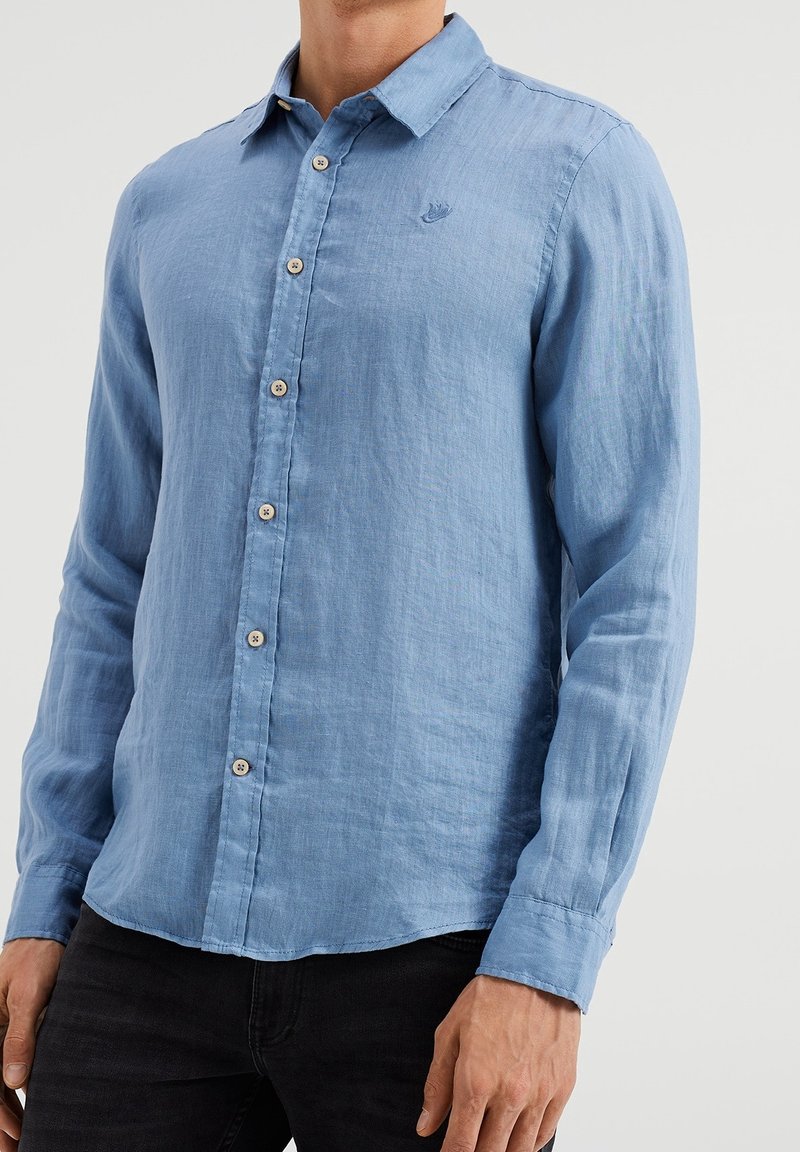 Ljusblå långärmad skjorta i linne med knappstängning fram, spetsig krage och en diskret broderad logotyp på bröstet.