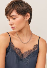 Navyblå satinkamisol med fin svart spetskant och tunna band, kombinerad med ett halsband av silverpärlor. Mjuk textur med detaljerad spets.