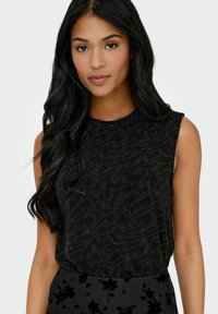 Czarny top bez rękawów z teksturowanym wzorem. Okrągły dekolt i miękki materiał, noszony z ciemnymi kwiatowymi spodniami o wzorze.