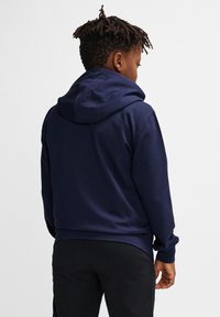 Marineblauer Hoodie mit einem Kordelzug, gerippten Bündchen und lockerer Passform, kombiniert mit schwarzen Hosen. Glatte Textur und minimalistisches Design.