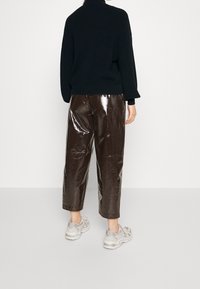 Maglione nero a maglia con colletto alto abbinato a pantaloni cropped in pelle sintetica lucida marrone. Indossato con sneaker grigio chiaro.