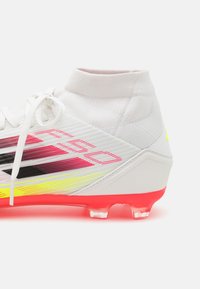 Cumpărătoare de fotbal alb cu accente multicolore în roz, negru și galben. Dispune de un guler tricotat, material texturat și o talpă roșie strălucitoare.