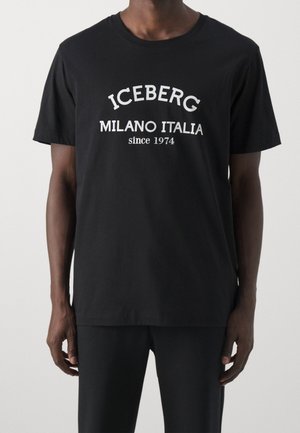 Mann trägt ein schwarzes kurzärmeliges T-Shirt mit weißem Text "ICEBERG MILANO ITALIA seit 1974" auf der Vorderseite, vor schlichtem hellem Hintergrund.