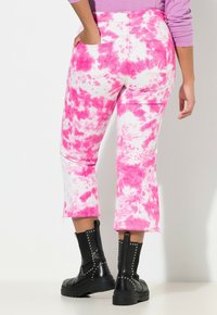 Jeans cortos de mezclilla con un diseño de tie-dye rosa y un dobladillo deshilachado, combinados con botas de tobillo negras con tachuelas. La vista trasera resalta los bolsillos.