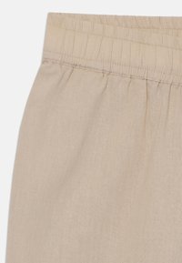 Tessuto di lino beige con una morbida texture, dotato di una vita elasticizzata e di dettagli arricciati nella parte superiore.