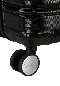 Valigia rigida nera con un design testurizzato, dotata di un accento in alluminio argentato e un alloggiamento per ruote nero resistente. Meccanismo di rotazione fluido.