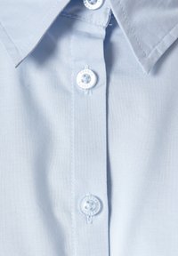 Jasnoniebieski kołnierzyk koszuli z dwoma białymi guzikami oznaczonymi "Fransa" na listwie, ukazujący fakturę materiału i szczegóły obszycia.