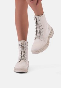Stivali alla caviglia beige chiaro in suede, con lacci frontali, occhielli metallici e suola in gomma testurizzata per una migliore presa.