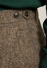 Brown tweed trousers featuring two dark buttons, a classic fit, and a textured fabric with subtle color variations.