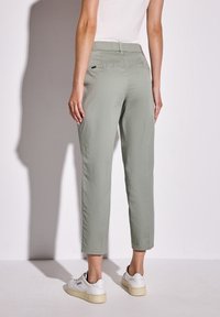 Pantalons cropped verts clairs avec une texture lisse, taille élastique et poches arrière, associés à des baskets blanches.