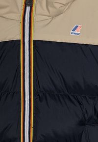 Giacca K-Way con parte superiore beige e parte inferiore blu navy. Presenta una zip frontale con strisce colorate e una trama trapuntata.