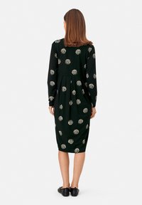 Dlouhý černý šat s bílými květinovými vzory, délka ke kolenům, vypasovaný pas a jemná, hladká textura.