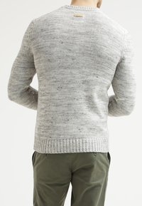 Pull gris en tricot texturé avec ourlet et poignets côtelés, agrémenté d'une petite patte à l'arrière du col. Associé à un pantalon vert.