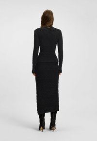 Długa czarna sukienka z fakturowanej tkaniny, z długimi rękawami i dopasowaną sylwetką, z spódnicą do kolan i delikatnymi wzorami.