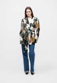 Kwiatowa, wielokolorowa marynarka z satynowej tkaniny, z paskiem w talii, długimi rękawami i dopasowanym krojem, zestawiona z niebieskimi jeansami.