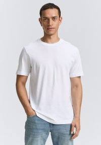 Camiseta blanca de algodón con mangas cortas y cuello redondo, combinada con jeans de color azul claro. La tela parece suave con un corte regular.