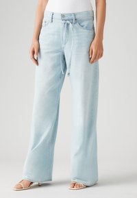 Lyseblå vide jeans i denim, med bånd i livet, knappelukking og frontlommer med en falmet tekstur.