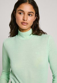 Menta zeleni, rebrasti džemper s turtleneck izrezom, dugih rukava i prilagođenog kroja, s suptilnim brendiranjem na prsima. Mekana tekstura.